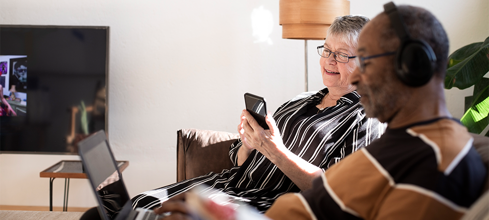Äldre kvinna som tittar i mobiltelefonen. Äldre man som använder laptop.